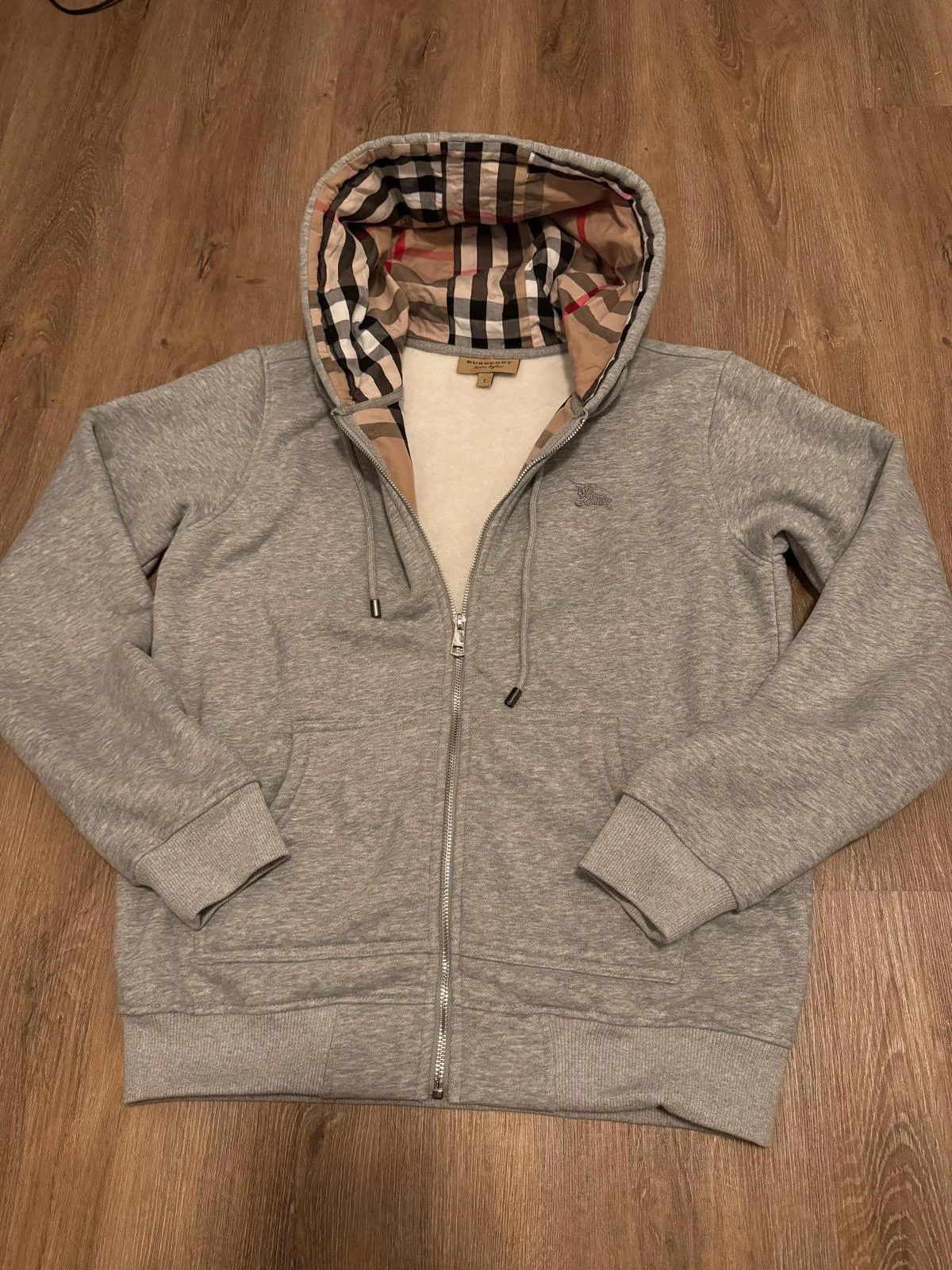 Sweat à capuche zippé gris avec doublure de capuche à carreaux.