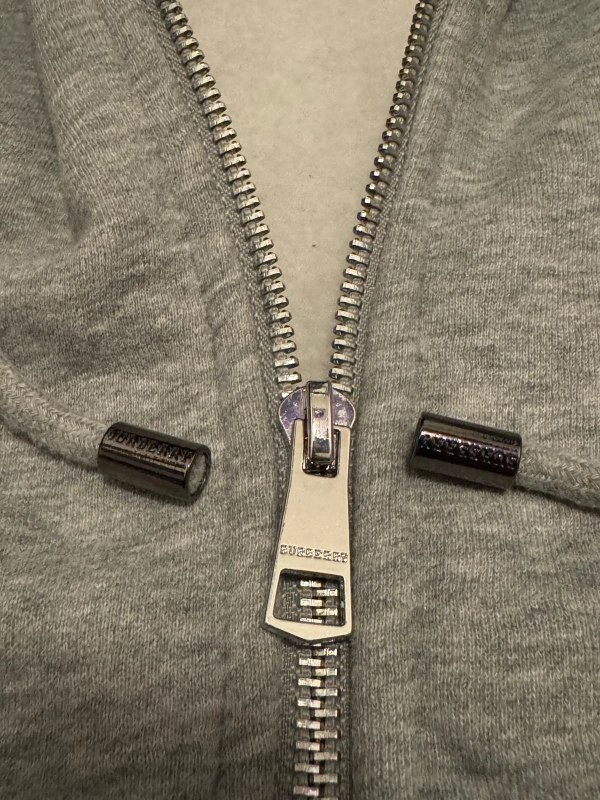 Détails zip et cordon de serrage sur le sweat à capuche gris.
